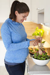 Schwangere Frau bereitet frischen Salat in der Küche zu - HMEF00586