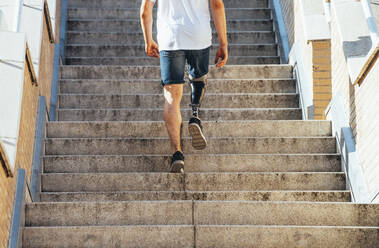 Young man with leg prosthesis walking upstairs - JCMF00220