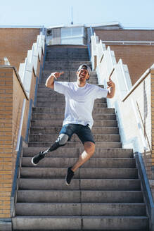 Fröhlicher junger Mann mit Beinprothese springt auf einer Treppe in der Stadt - JCMF00221