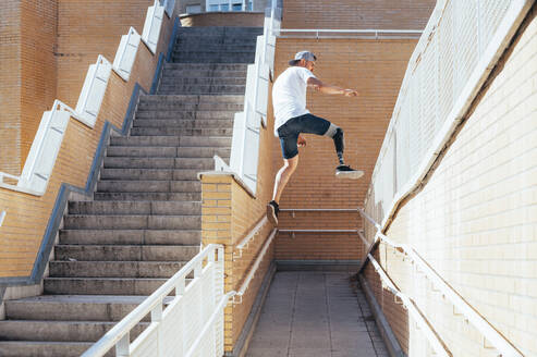 Junger Mann mit Beinprothese beim Parkour in der Stadt - JCMF00222