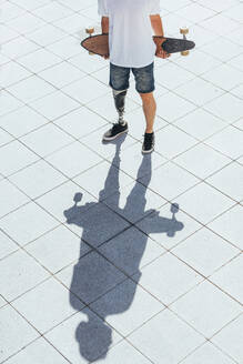 Junger Mann mit Beinprothese hält Skateboard - JCMF00224