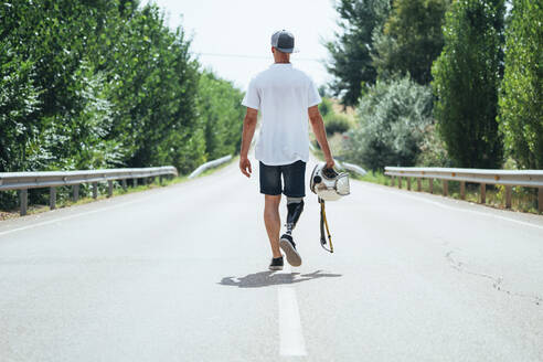 Junger Mann mit Beinprothese, der mit einem Helm die Straße entlanggeht - JCMF00225