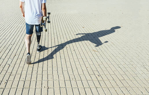 Junger Mann mit Beinprothese geht und hält Skateboard - JCMF00226