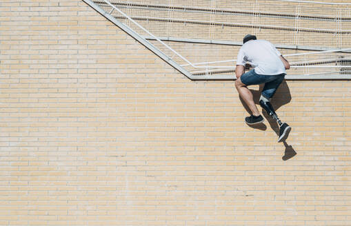 Junger Mann mit Beinprothese klettert an einer Ziegelmauer hoch - JCMF00232