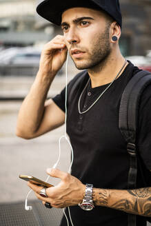Junger Mann mit Kopfhörern und Smartphone in der Stadt - GIOF07164