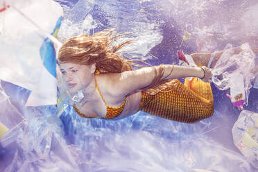 Teenage mermaid girl diving through plastic waste under water - STBF00397