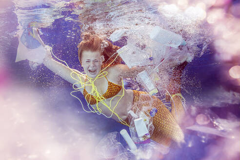 Screaming teenage mermaid girl surrounded by plastic waste under water - STBF00402