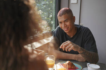 Porträt eines jungen Mannes, der mit seiner Freundin in einem Café frühstückt - MCVF00039