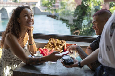 Portrait of smiling woman paying with smartphone at coffee shop - MCVF00041