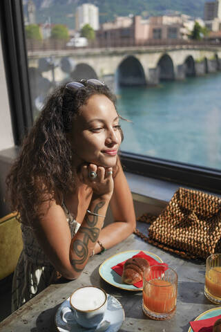 Porträt einer lächelnden jungen Frau, die am Frühstückstisch in einem Café sitzt, Lecco, Italien, lizenzfreies Stockfoto