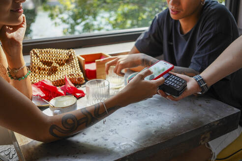 Junge Frau bezahlt Rechnung mit Smartphone in einem Café - MCVF00044