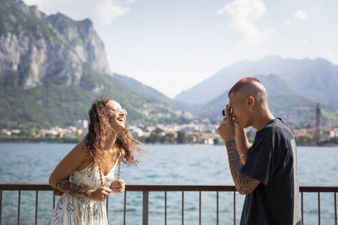 Junger Mann fotografiert seine Freundin vor dem Comer See, Lecco, Italien - MCVF00051