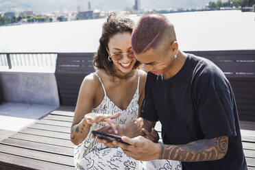 Glückliches junges Paar, das auf sein Handy schaut, Lecco, Italien - MCVF00053
