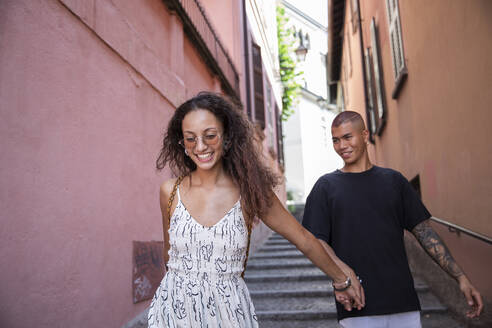 Porträt einer glücklichen jungen Frau, die mit ihrem Freund durch eine Gasse geht, Lecco, Italien - MCVF00056