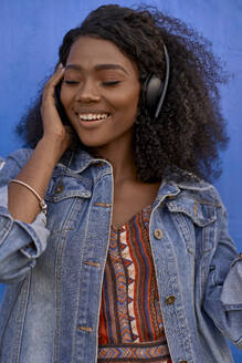 Porträt einer lächelnden jungen Frau, die mit Kopfhörern Musik hört - VEGF00725