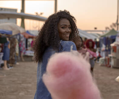 Portrait of happy young woman with pink candyfloss on street market - VEGF00728