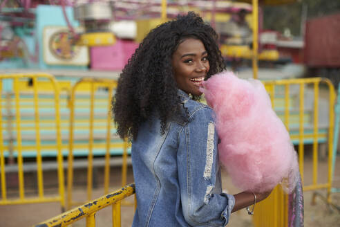 Porträt einer glücklichen jungen Frau mit rosa Zuckerwatte auf dem Jahrmarkt - VEGF00731