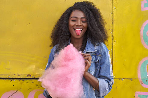 Portrait of smiling young woman with pink candyfloss sticking out tongue - VEGF00736