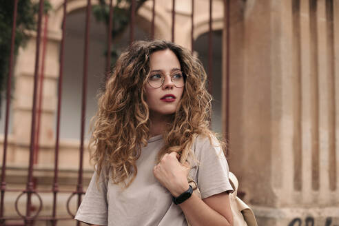 Beautiful young woman with curly hair and glasses in the city - LOTF00073