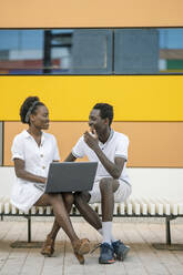 Young couple sitting on bench with laptop - DLTSF00186