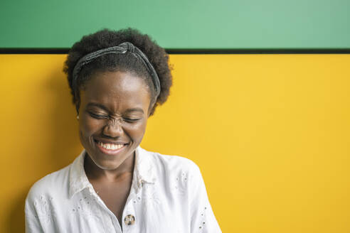Portrait of laughing young woman in front of yellow and green wall - DLTSF00208