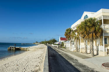 Colonial houses in front of beach against blue sky during sunny day at Cockburn town, Grand Turk - RUNF03226