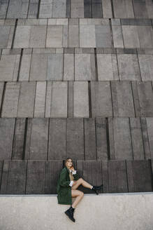 Blonde junge Frau mit grüner Jacke sitzt auf einer Mauer, Wien, Österreich - LHPF00958