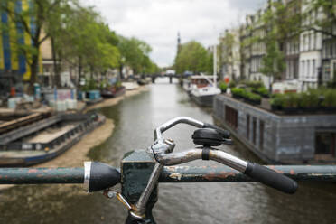 Niederlande, Amsterdam, Lenker eines am Geländer einer Grachtenbrücke abgestellten Fahrrads - XCF00237