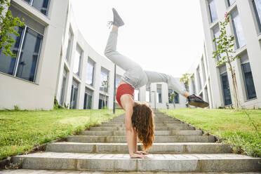 Young woman doing a handstand on outdoor stairs - JSMF01272