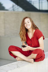 Portrait of smiling sporty young woman having a break using smartphone outdoors - JSMF01276