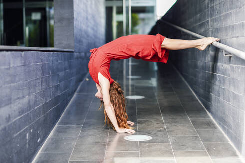 Sporty young woman doing acrobatics at a passageway - JSMF01288