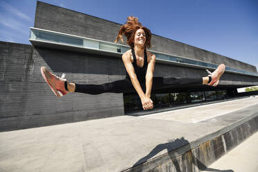 Happy sporty young woman jumping at a modern building - JSMF01290