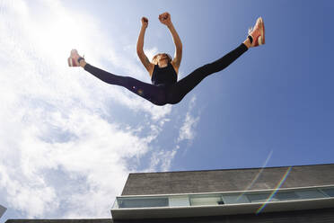 Sporty young woman jumping outdoors in sunlight - JSMF01291