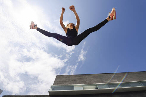 Sportliche junge Frau, die im Freien im Sonnenlicht springt - JSMF01291
