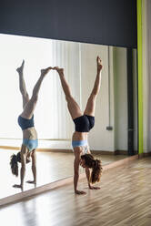 Sporty young woman doing a handstand in exercise room - JSMF01315