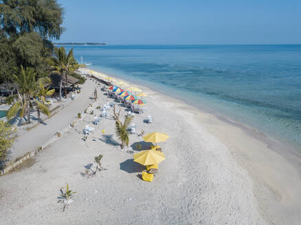 Drohnenansicht von Stühlen und bunten Sonnenschirmen, die auf der Insel Gili-Air vor einem klaren blauen Himmel aufgestellt sind, Bali, Indonesien - KNTF03497