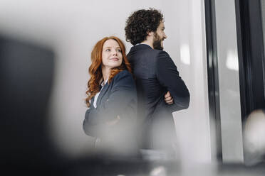 Selbstbewusster Geschäftsmann und Geschäftsfrau stehen Rücken an Rücken im Büro - KNSF06587