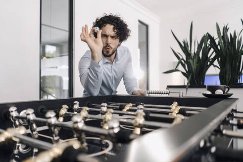 Businessman with ball at foosball table in office - KNSF06595