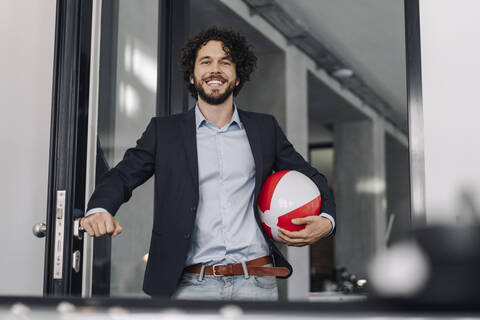 Glücklicher Geschäftsmann hält Strandball im Büro, lizenzfreies Stockfoto