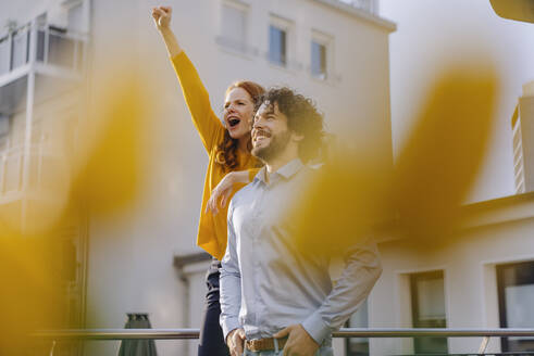 Woman with colleague on roof terrace clenching fist - KNSF06600