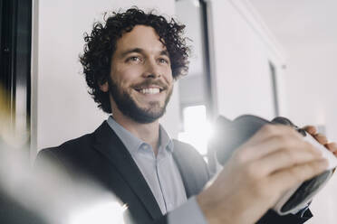 Portrait of smiling businessman holding VR glasses in office - KNSF06605