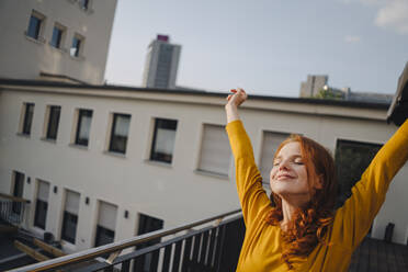 Smiling redheaded woman stretching on roof terrace - KNSF06617