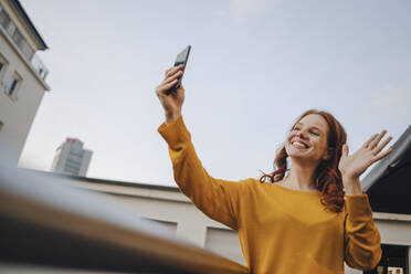Lächelnde rothaarige Frau benutzt Handy auf Dachterrasse - KNSF06620