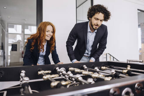 Businessman and businesswoman playing foosball in office - KNSF06622