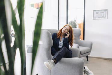 Redheaded businesswoman on the phone in armchair - KNSF06636