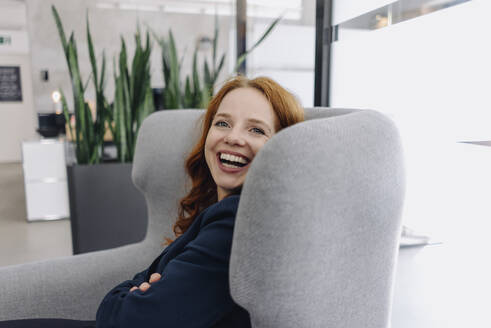 Happy redheaded businesswoman sitting in armchair - KNSF06637