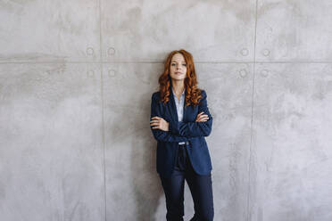 Portrait of confident redheaded businesswoman standing at a wall - KNSF06638