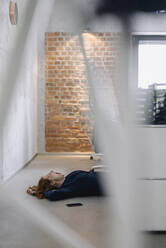 Müde Geschäftsfrau auf dem Boden liegend im Büro - KNSF06643