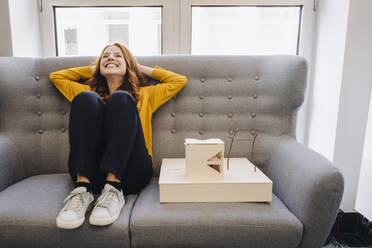 Happy woman sitting on couch next to architectural model - KNSF06652