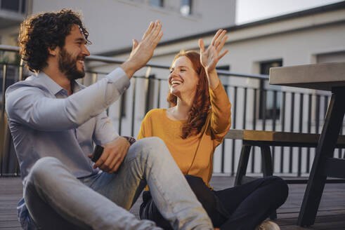 Two happy colleagues high fiving on roof terrace - KNSF06657